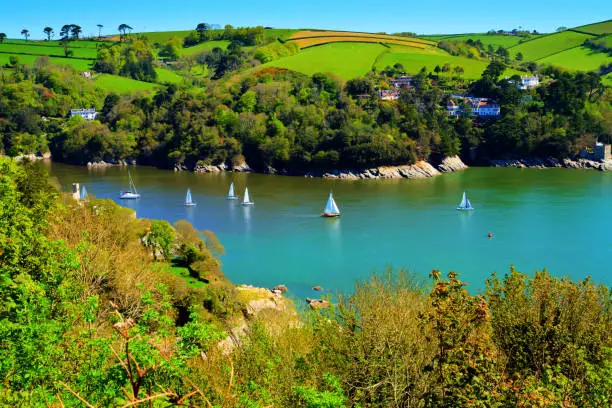 Yachts sailing Devon coast calm blue sea Dart estuary near Dartmouth in beautiful weather with colourful countryside