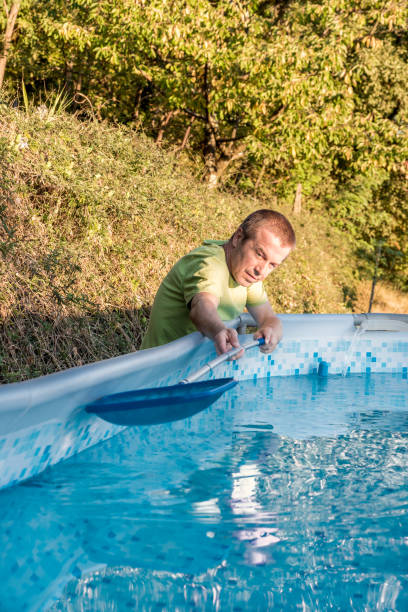 istock Man in Backyard Cleaning Portable Swimming Pool with a Net to Remove Leaves and Insects from the Water 1351908164