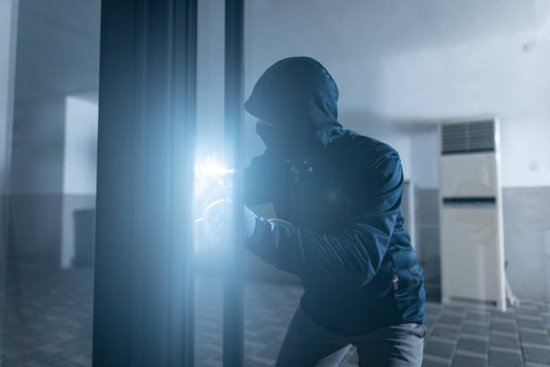 istock Thief holding flashlight and trying to open glass door and break into office 1351912413