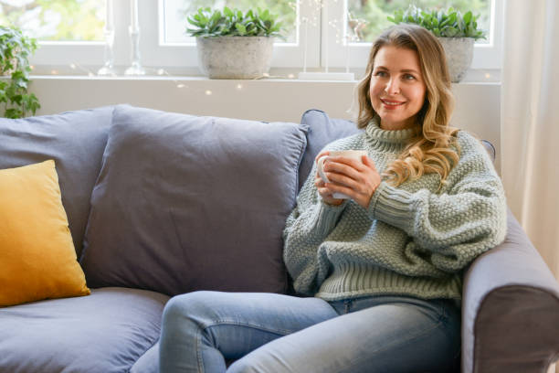 istock attractive middle aged woman sitting on the couch (drinking hot tea) 1351913835
