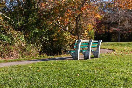 One bench nest to a walking path facing colorful Autumn leaves in a park that leads to SOuthards Pond and Belmont Lake in Babylon New York.