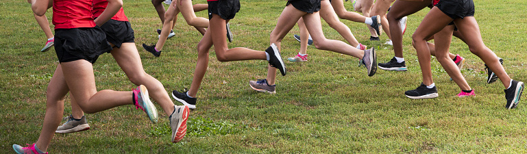 Close up of a side view of the start of a girls high school cross country race on a grass field at Van Cortlandt Park in the Bronx New York.