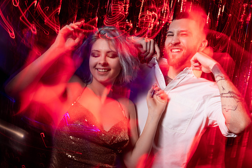 Party vibe. Excited couple. Birthday fun. Festive celebration. Happy expressive man and woman enjoying holiday long exposure black red light motion ornament waves blur.