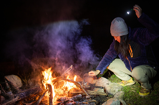 A Japanese woman cooking on a cast iron skillet over an open camp fire.