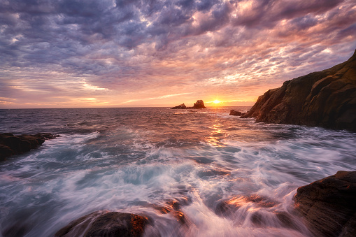 Waves crash over the rocks on a high tide, and the sun winks through the clouds as an approaching storm looms at Crescent Bay, Laguna Beach in Southern California