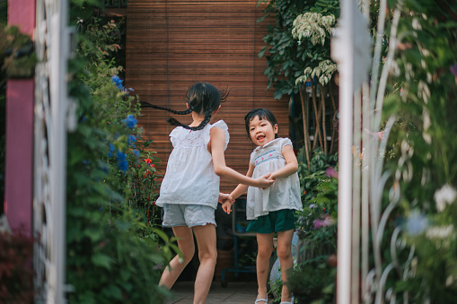 2 asian chinese young sisters holding hands jumping around at front yard of the house during weekend evening laughing having fun time together