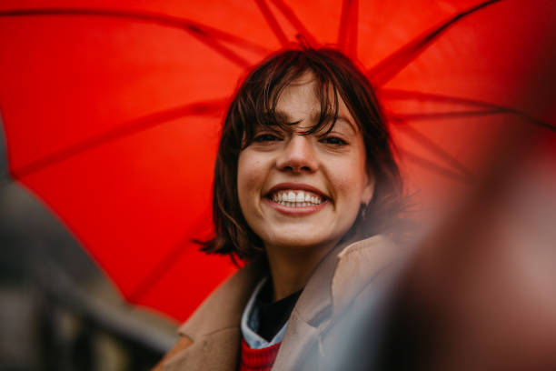 Shot of a young woman taking a selfie while walking outdoors on a rainy day with a red umbrella.