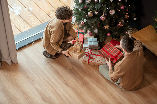 Above view of married couple sitting on floor and putting gifts inbeautiful wrappings under Christmas tree