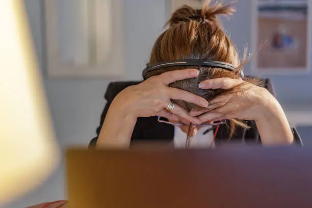 Photo of Dejected middle-aged woman - working at home using laptop and headphones with microphone - screaming of hopelessness by emotional stress caused by oppressive job. Madrid, Spain