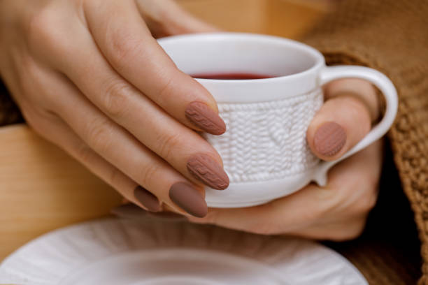 Stylish winter nail design. Knitted fabric texture on women's nails. A woman's hand holds a cup of warm drink Stylish winter nail design. Knitted fabric texture on women's nails. A woman's hand holds a cup of warm drink. Close-up nails. fall nail art stock pictures, royalty-free photos & images