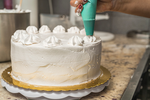 Close up view of a female pastry chef garnishing a white cake with cream using a piping bag