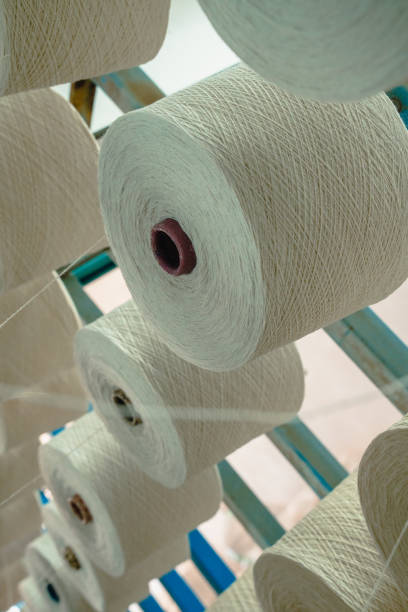 istock White yarn spools bobbin thread cones on industrial warping knitting beaming machine in textile factory 1351977235