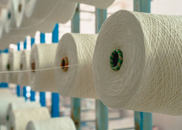 istock White yarn spools bobbin thread cones on industrial warping knitting beaming machine in textile factory 1351977249