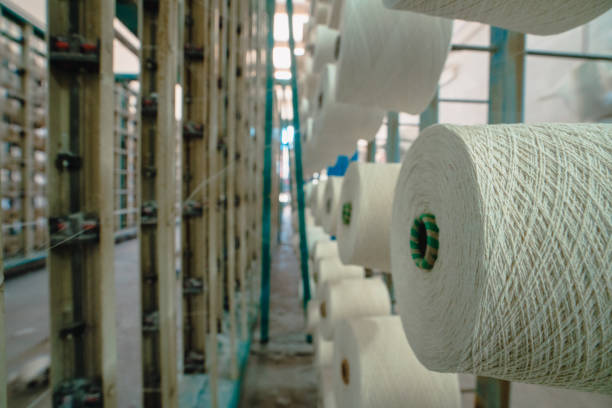 istock White yarn spools bobbin thread cones on industrial warping knitting beaming machine in textile factory 1351977257