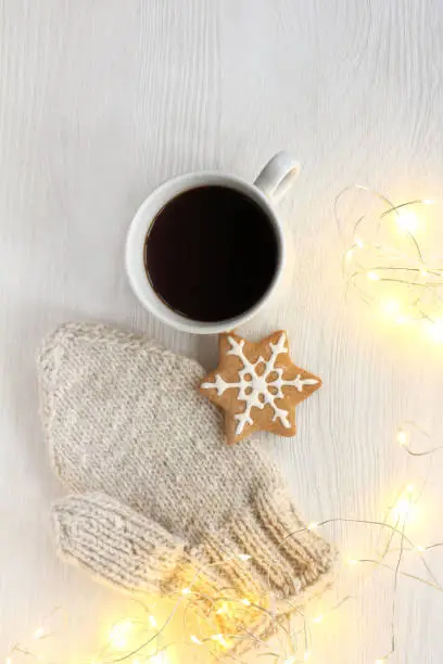 black coffee in a cup, ginger snowflake and knitted mitten with lights included garland top view