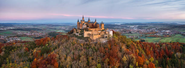 Hohenzollern Castle in Autumn Sunrise Panorama Burg Hohenzollern Castle Germany Bisingen, Baden Württemberg, Germany - October, 25th 2020: Swabian Jura Germany Autumn Aerial Panorama with Hohenzollern Castle - Burg Hohenzollern 15th century hilltop castle in sunrise light in autumn season. Colorful surrounding autumn colored trees around the hill of Burg Hohenzollern, view to the surrounding cities of Hechingen, Bisingen and Tübingen on the horizon. Aerial Drone Point of view stiched XXXL Panorama. Swabian Jura, Baden Württemberg, Southwest Germany, Germany, Europe. reutlingen photos stock pictures, royalty-free photos & images