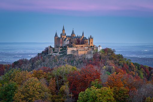 Bisingen, Baden Württemberg, Germany - October, 25th 2020: Hohenzollern Castle - Burg Hohenzollern hilltop castle in early sunrise light during autumn. Colorful autumn colored forest trees around the hill of Burg Hohenzollern. Swabian Alb, Baden Württemberg, Southwest Germany, Germany, Europe.