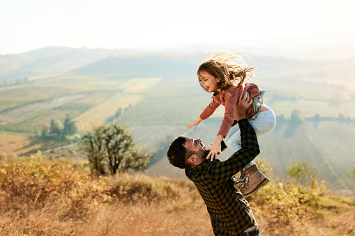 Carefree single father having fun while throwing his daughter high up in nature. Copy space.