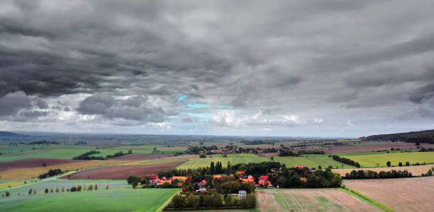istock Cloudy sky over small village in the slightly hilly landscape with fields and meadows in Germany, aerial photo 1351985833