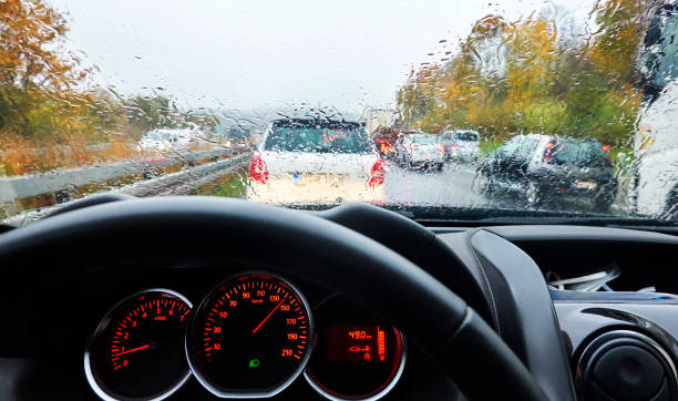 vista sul cruscotto di un'auto attraverso il parabrezza smorzato dalla pioggia del traffico sull'autostrada in germania - car steering wheel windshield speedometer foto e immagini stock