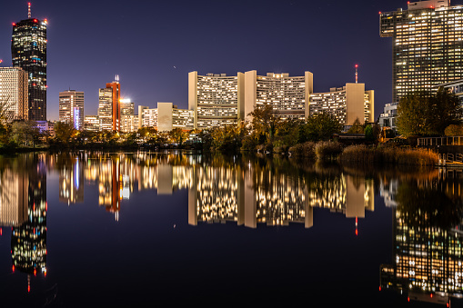 Illuminated Buildings of Business District in the City of Vienna Austria in Twilight with Skyline Reflecting in Water of River Danube at Clear Evening Sky