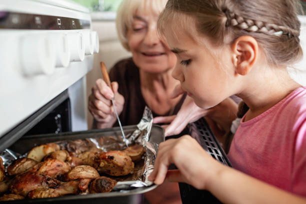 Granny and small girl take pan with baked roast chicken and potato out of oven, together in kitchen Excited caring grandmother and concentrated small girl taking pan with baked roast chicken and potato out of oven, together in the kitchen, cooking for family dinner, home lifestyle duck family stock pictures, royalty-free photos & images