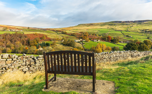 Swaledale, Arkengarthdale. A wooden bench with long distant views across the dale in Autumn with remote hill farms and home steads.  Landscape.  Space for copy.