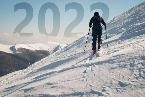 Man climbing a mountain on touring skis with new year 2022 ahead. Active new years resolution concept.