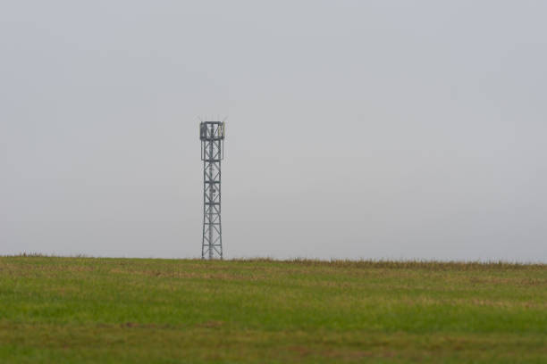 Mobile cell tower antenna mast providing mobile internet connection for rural area standing on empty barren field on grey overcast dark moody day