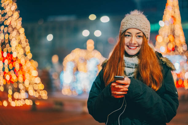 Portrait Caucasian woman sitting on sofa with smartphone and wireless headphones, enjoying music during Xmas holidays.