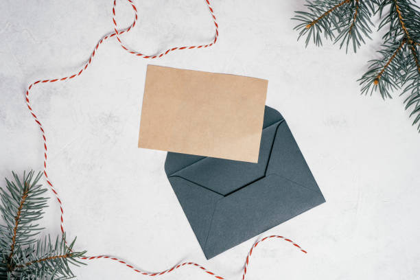 istock Green open Christmas envelope on white concrete background with blank kraft paper greeting card. Copy space. Top view 1351990611