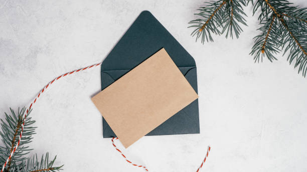istock Green open Christmas envelope on white concrete background with blank kraft paper greeting card. Copy space. Top view 1351990614