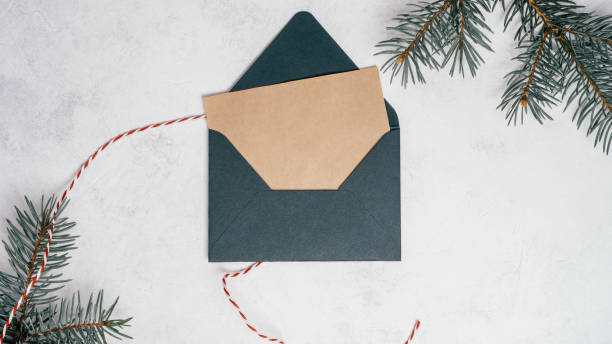 Green open Christmas envelope on white concrete background with blank kraft paper greeting card. Copy space. Top view stock photo