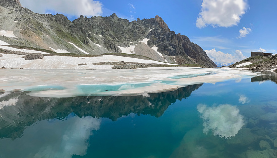 beautiful clear water of an alpine lake and ice with sky  reflection and rocky mountain around