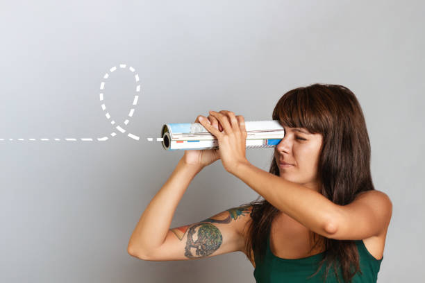 The concept of finding new solutions and opportunities. A beautiful young woman looks through a telescope at a rolled-up newspaper or magazine The concept of finding new solutions and opportunities. A beautiful young woman looks through a telescope at a rolled-up newspaper or magazine. rolled up magazine stock pictures, royalty-free photos & images