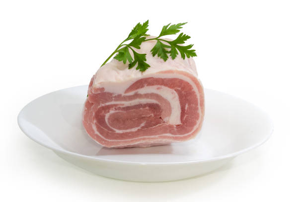 Coiled piece of the frozen streaky pork belly with fresh parsley twig on a white dish on a white background
