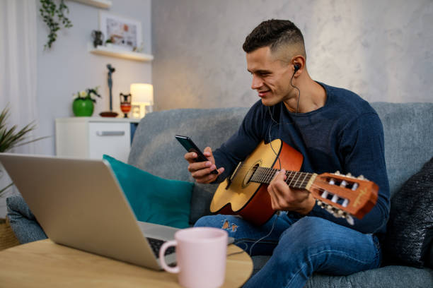 istock Young man using smart phone and looking up chords for a song he is learning to play 1351997538