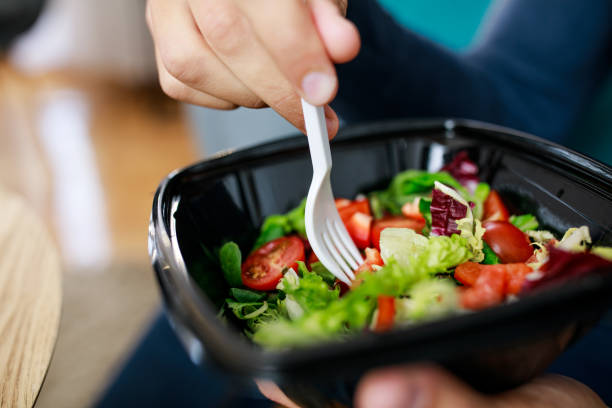 hombre irreconocible disfrutando de una saludable ensalada para llevar para el almuerzo - plastic knife fotografías e imágenes de stock