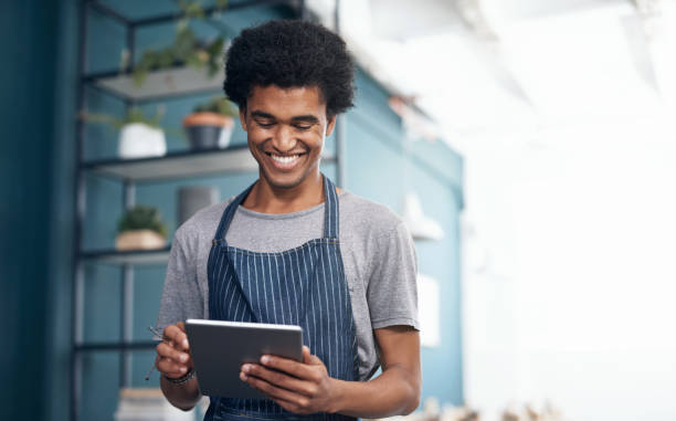 istock Shot of a handsome young waiter standing alone in his cafe and using a digital tablet 1351999744