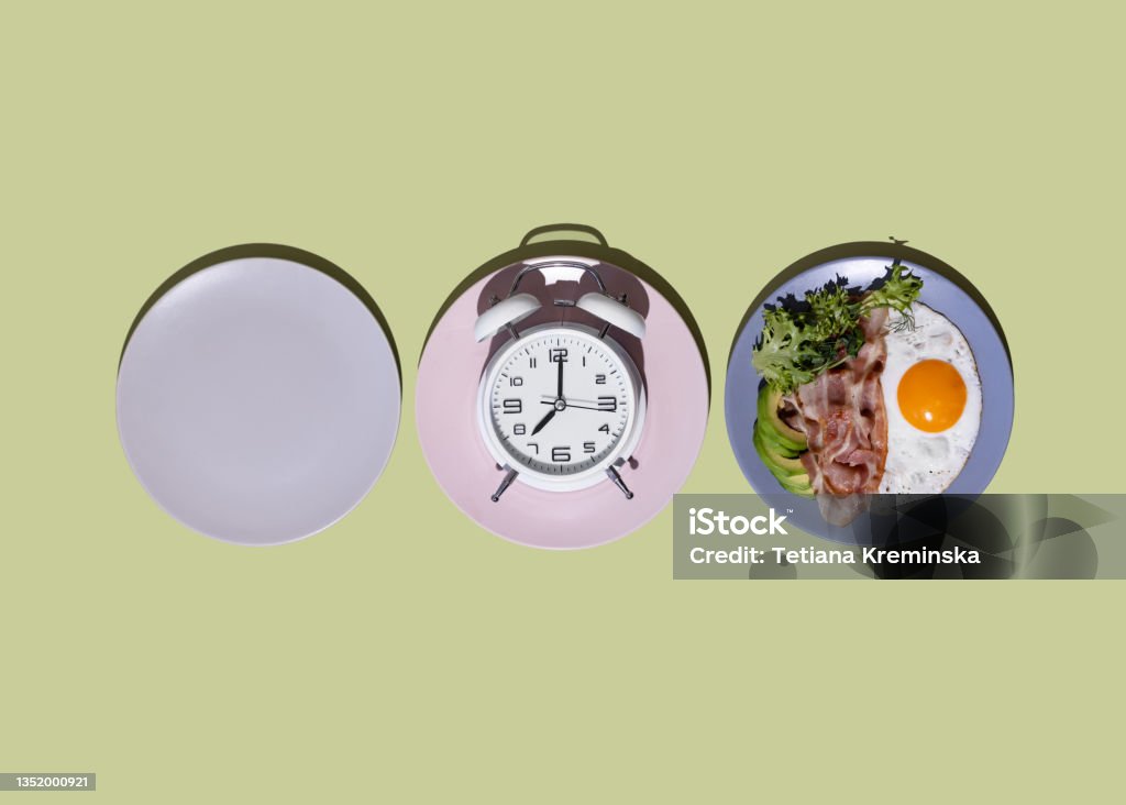 Intermittent fasting concept with blank colorful plates. Healthy keto breakfast - bacon, fried eggs, avocado and microgreens. Low in carbohydrates, high in fat. Intermittent fasting concept with blank colorful plates. Healthy keto breakfast - bacon, fried eggs, avocado and microgreens. Low in carbohydrates, high in fat. Top view. Intermittent Fasting Stock Photo