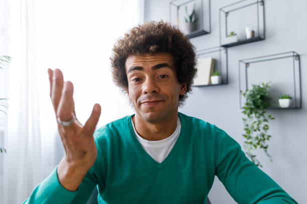 Young mixed race man gesturing while video chatting with a friend Personal perspective of smiling young man looking at camera as if he is on a video conference call and gesturing while talking to a friend. man video call pov stock pictures, royalty-free photos & images