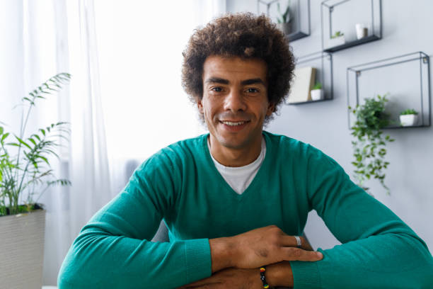 Young man smiling at camera during a video call with a friend Personal perspective shot of cheerful young man sitting in his living room and having a video conference with a friend. He is looking and smiling at camera. man video call pov stock pictures, royalty-free photos & images