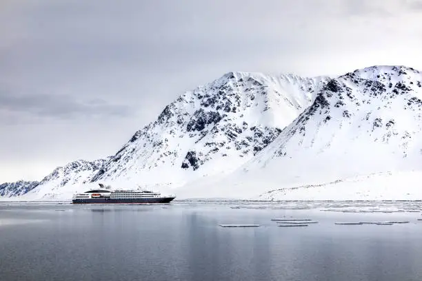 Photo of Pristine snow covered mountains of Svalbard with tourist cruise ship in the fiord. Ecotourism is becoming popular in the region