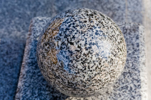 Polished granite ball made with light gray granite as architectural element of the decoration, top view close-up on a blurred background