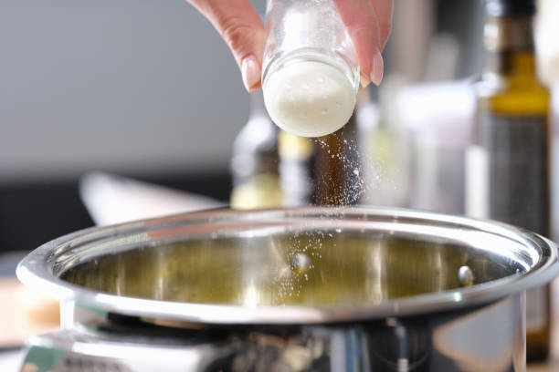 Chef pours salt into a saucepan with food, hands close-up stock photo