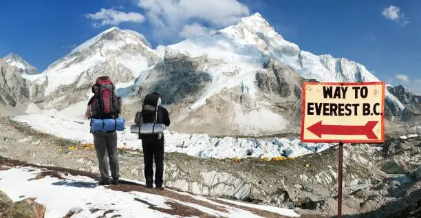 Panoramic view of Mount Everest base camp with two tourists and signpost way to Everest b.c. Sagarmatha national park, Khumbu valley Solukhumbu - Nepal Himalayas mountains