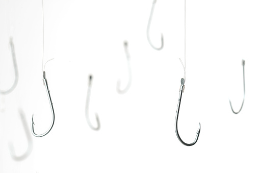 Fishing hooks are hanging with transparent string in front of white background.