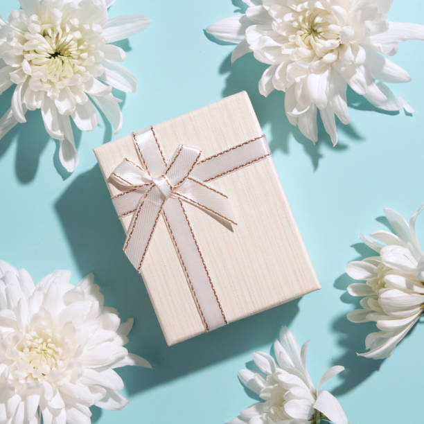 istock White flowers and present or gift box on blue pastel table top view 1352007910