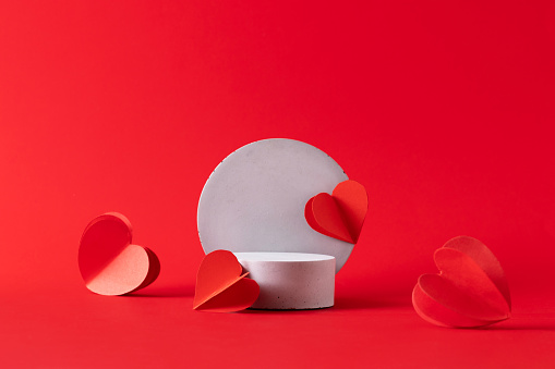 Gray podium with red hearts on vibrant red background to show cosmetic products. Minimal romantic backdrop with stand for branding and presentation on Valentine's Day.