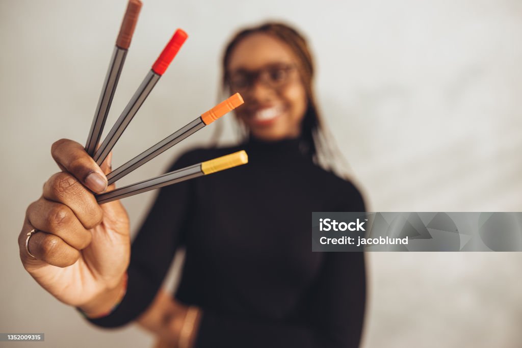 Creative designer holding coloured pens Creative designer holding coloured pens while smiling cheerfully in the background. Happy young freelancer standing alone in her home offie. Artistic young woman working on a new project. One Woman Only Stock Photo